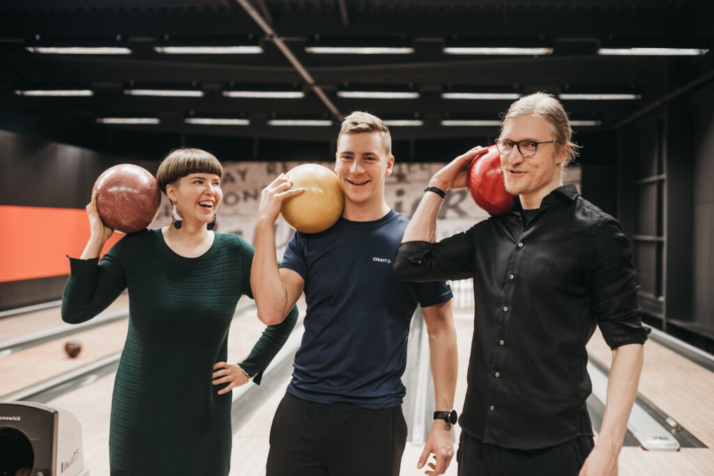 Three people smiling at the cameta holding bowling balls